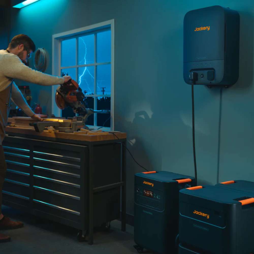 Jackery Battery Pack 5000 Plus powering a home workshop with a wall-mounted energy system while a person operates a power saw indoors