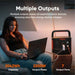 Jackery Explorer 2000 V2 Portable Power Station sits beside a woman using a laptop, showing multiple output ports for powering home devices during an outage