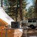 Jackery HomePower 3000 Portable Power Station powers an espresso machine on a camping table beside a large tent in a forest campsite