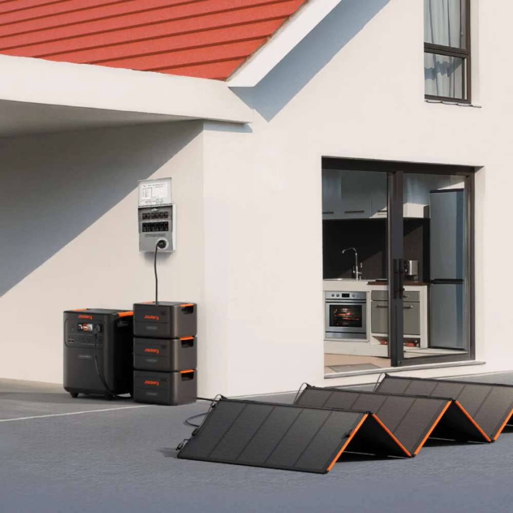 Jackery HomePower 3600 Plus Battery Pack stacked beside a Jackery power station and solar panels outside a house