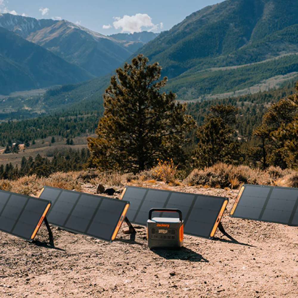 Jackery SolarSaga 200W Solar Panel charging a portable power station outdoors, surrounded by multiple solar panels with mountains in the background