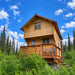 Tall Jumbo Grand Loft 130 SD cabin with an upper loft window, wooden balcony and steps surrounded by lush greenery.