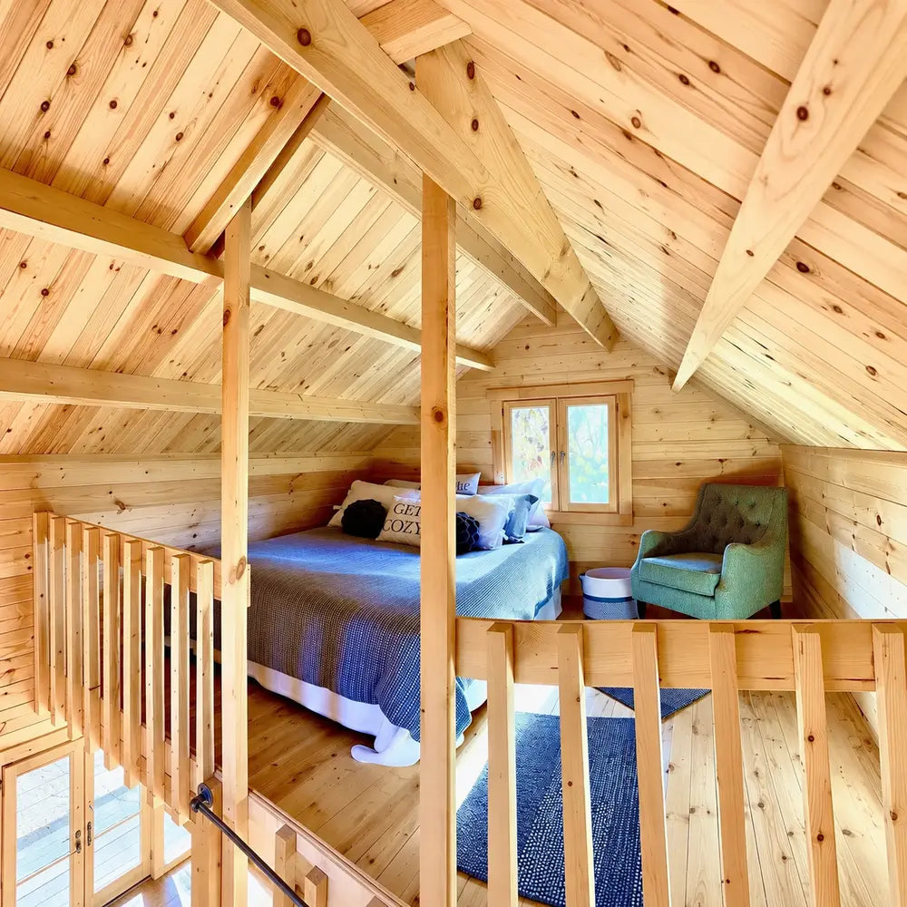 Furnished Jumbo Grand Loft 130 SD sleeping loft with Get Cozy pillows, a green reading chair, wooden railings and exposed ceiling beams.