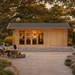 Rectangular wood cabin with glass doors and a bar inside, set on a stone patio with people sitting at a table.
