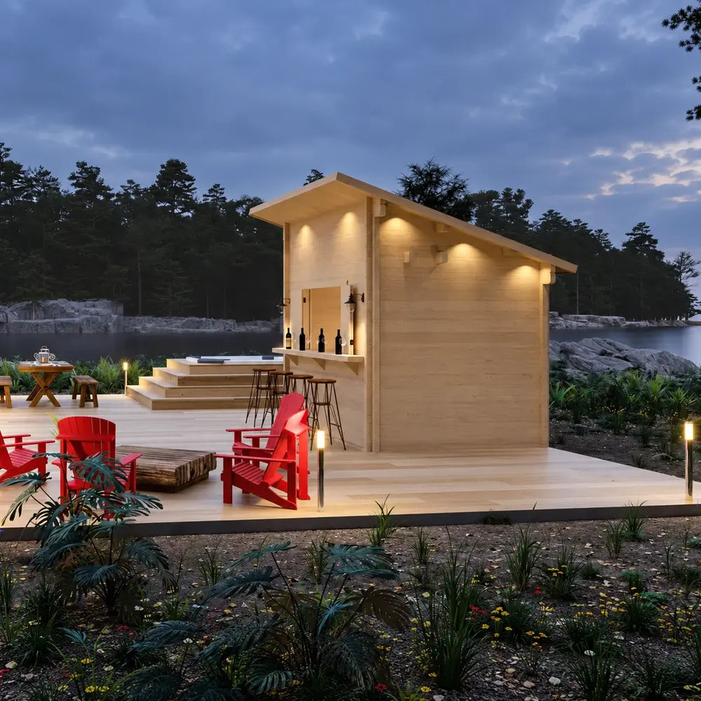 Natural-wood Lakeside Versa Cabana 67 glowing with warm exterior lights on a landscaped lakeside deck at dusk with red Adirondack chairs.
