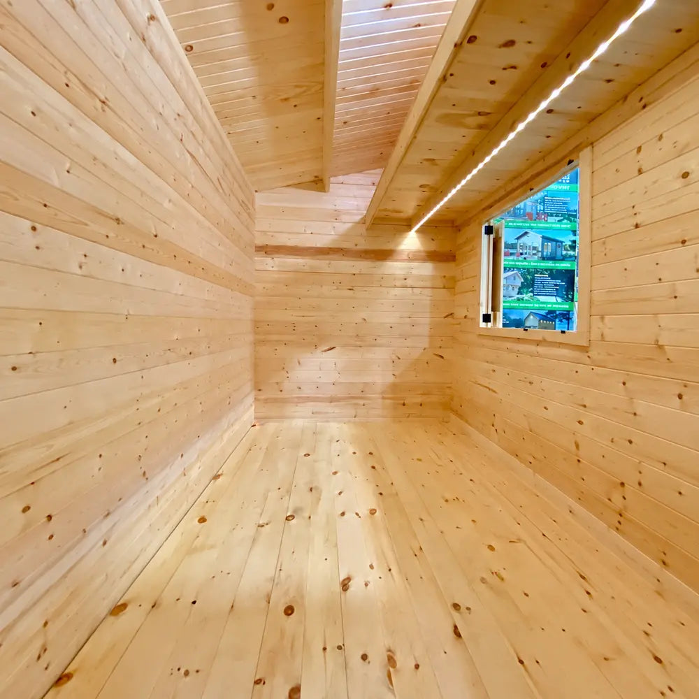 Long, narrow interior of the Lakeside Versa Cabana 67 featuring pine plank walls, a spacious wooden floor, exposed ceiling beams, and a serving window.