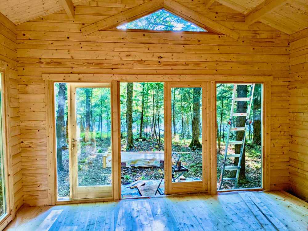Large glass doors let sunlight pour into the unfinished Sawmill Structures Edwin Lake House 70MM Garden Room