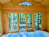 Large glass doors let sunlight pour into the unfinished Sawmill Structures Edwin Lake House 70MM Garden Room