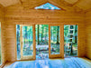 Large glass doors let sunlight pour into the unfinished Sawmill Structures Edwin Lake House 70MM Garden Room