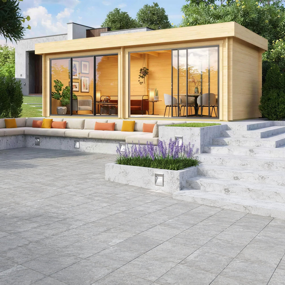 GardenHouse24 USA Lasse 44A ALU Garden Room is set up in a landscaped garden with furniture inside, appearing as a stylish home office or lounge