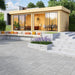 GardenHouse24 USA Lasse 44A ALU Garden Room is set up in a landscaped garden with furniture inside, appearing as a stylish home office or lounge