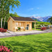 Lerum 44 wooden garden room with a covered porch, two hanging egg chairs and an outdoor kitchen, set in a landscaped garden against snow-capped mountains.