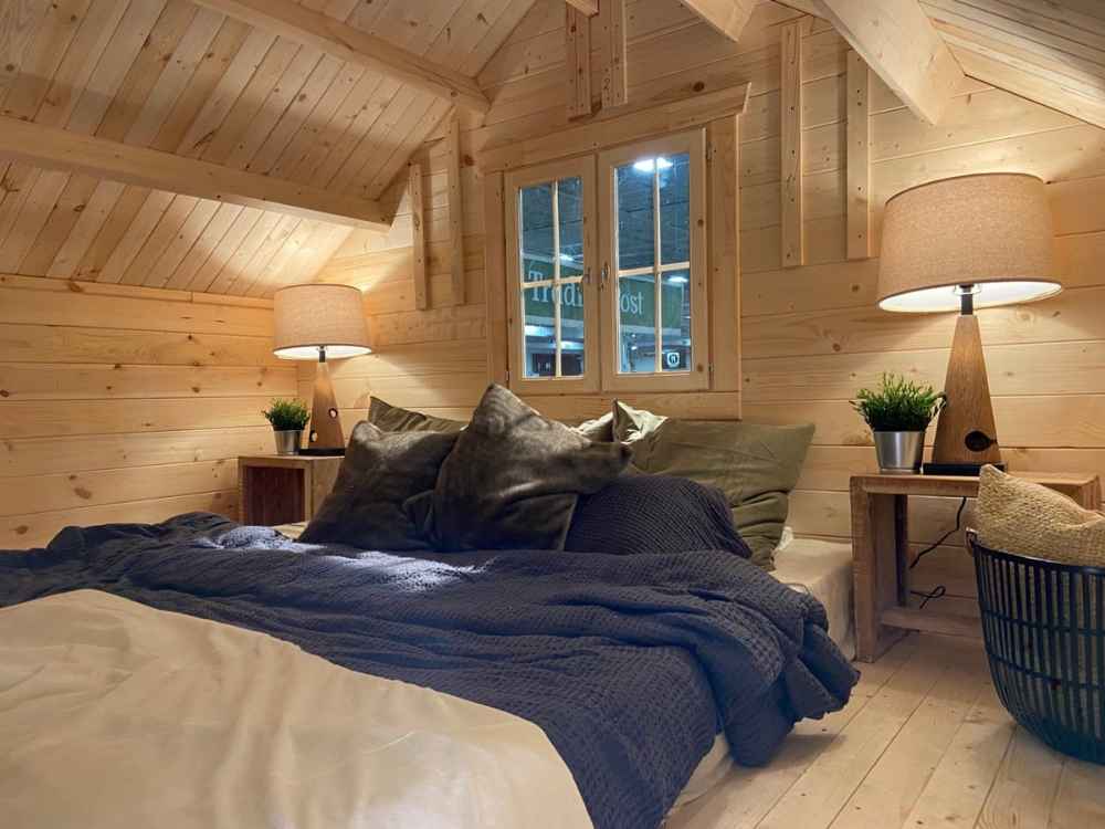 Loft bedroom of the Sawmill Structures Grand Loft 107 Deluxe DD Garden Room is softly lit with two bedside lamps, showcasing a double bed and wood-paneled slanted ceiling