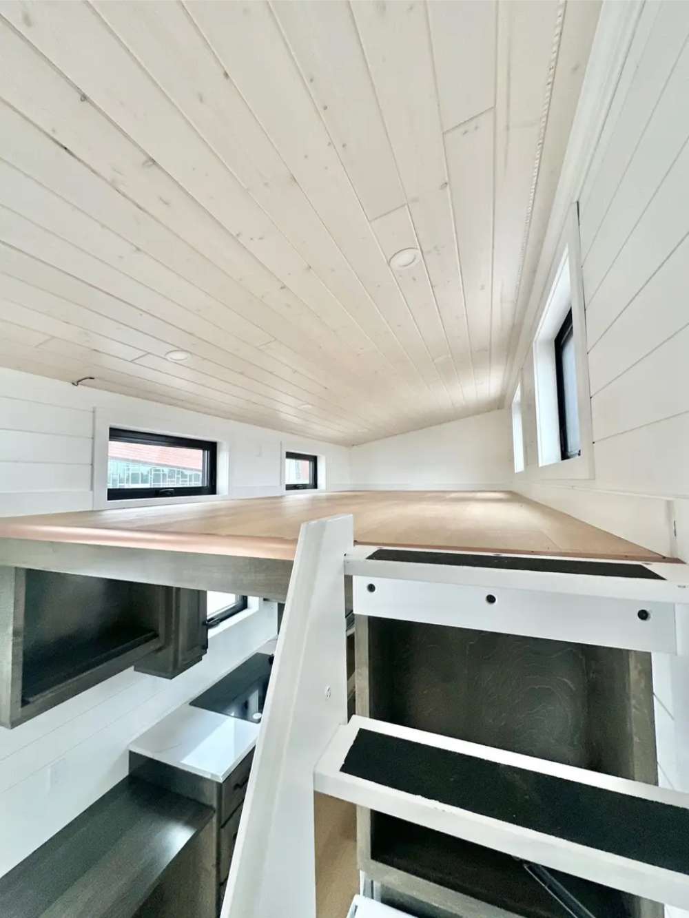 Loft in Sawmill Structures Wanderlove Tiny Home offers a low-ceiling sleeping area with natural light from several windows and a wood-paneled ceiling