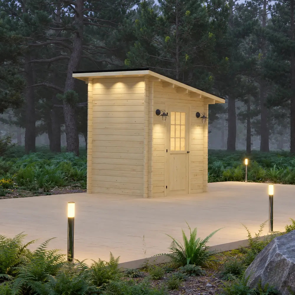 Angled dusk view of the pale wood Loo Loo House with a sloped roof, glazed door, black sconces, roof downlights, and illuminated pathways in a misty forest.