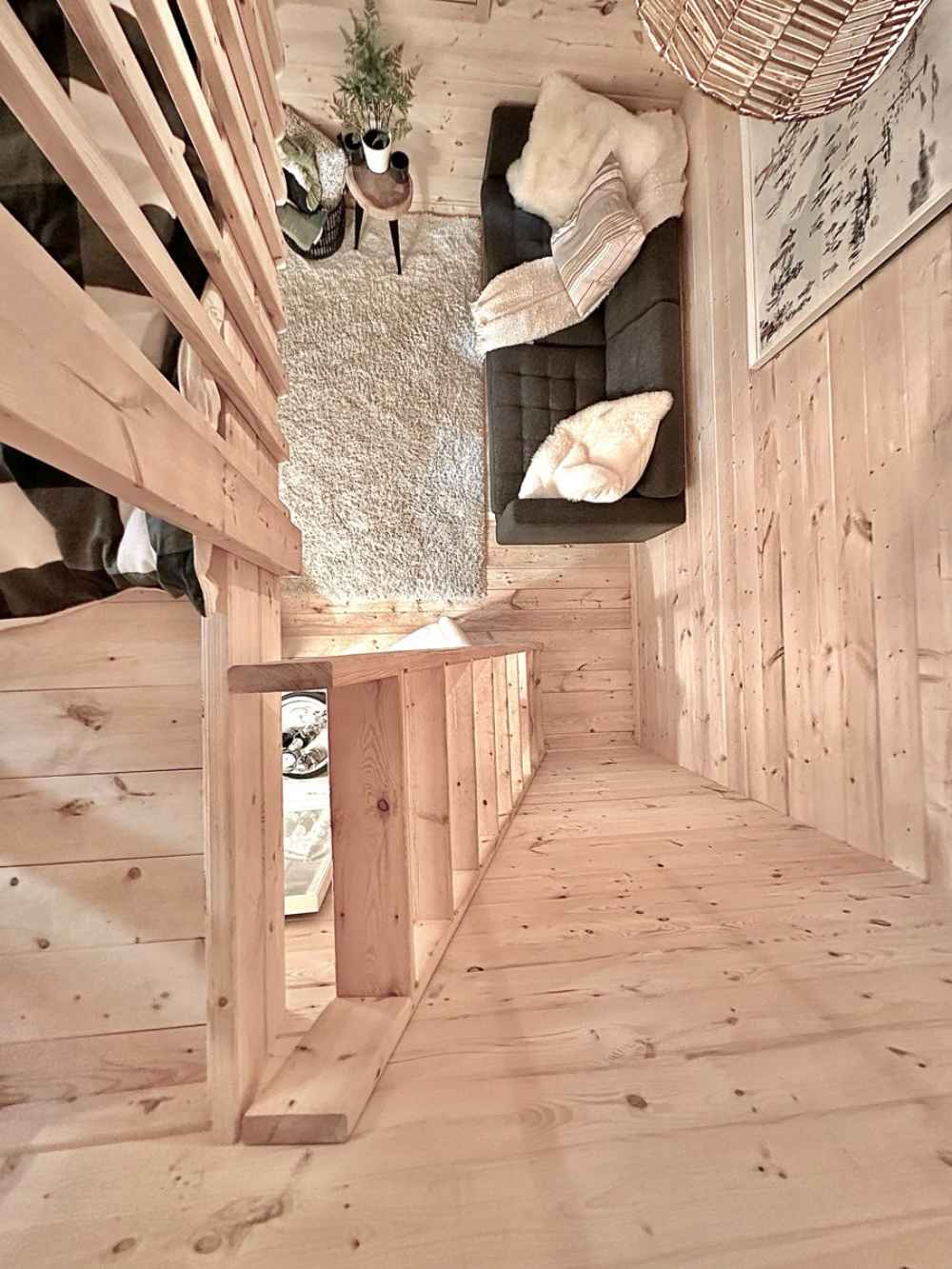 Looking down from the loft, a cozy living room with a dark couch, fluffy rug, and greenery is part of the Sawmill Structures Ontario Grand Loft 107 SD Garden Room