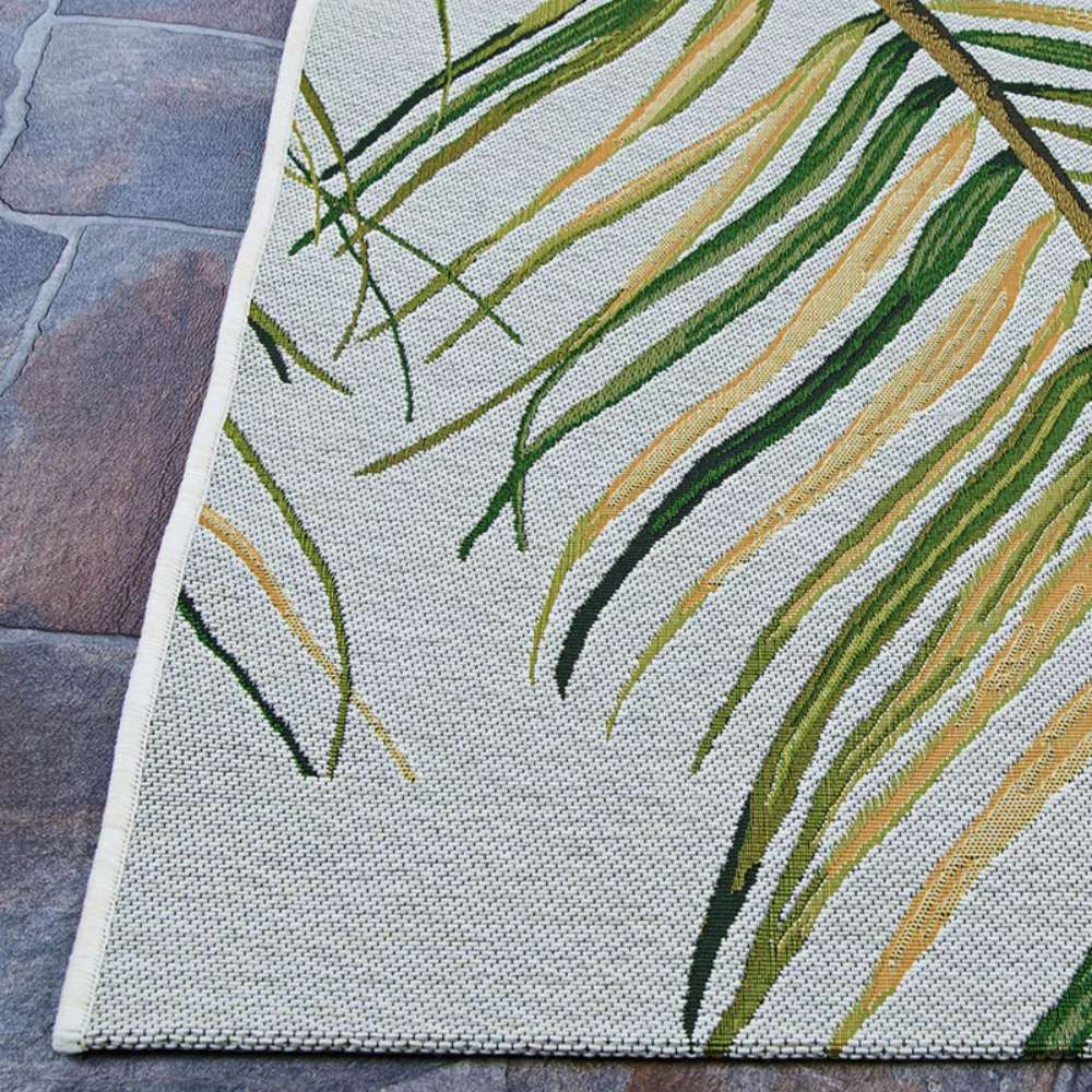 Lower left corner of Couristan Dolce Indoor/Outdoor Rug - Bamboo Forest/Frost rests on stone flooring with long green and yellow leaves woven