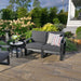 LuxCraft Lanai Deep Seating Loveseat featuring charcoal gray cushions and black wooden armrests, sits elegantly in an outdoor space surrounded by greenery and light