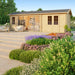 A staged outdoor scene with chairs, flowers, and a cozy reading nook showcases the GardenHouse24 USA Mikelli 44 Garden Room as an inviting retreat