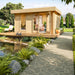 A lifestyle image of the GardenHouse24 USA Miriam 44A Modern Garden Room set in a lush backyard with open doors and cozy furnishings inside