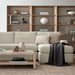 Modern living room uses Crate & Barrel Terrazza 114" Natural Solid Oak Wood 5-Shelf Bookcases, Set of 3 as a stylish backdrop behind a cream sectional sofa