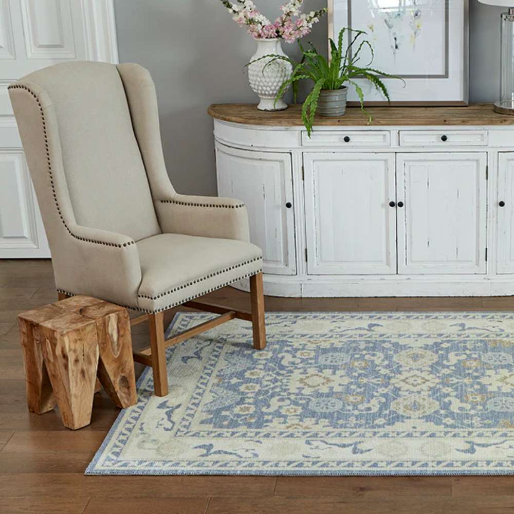 Momeni Anatolia Indoor Rug - ANA-7 Light Blue adds elegance to a cozy room with a beige armchair, wooden stool, and white cabinet
