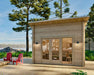 Morning light glows on the Sawmill Structures The Versa 107 70MM Garden Room, a small wooden cabin nestled by the lake with chairs placed