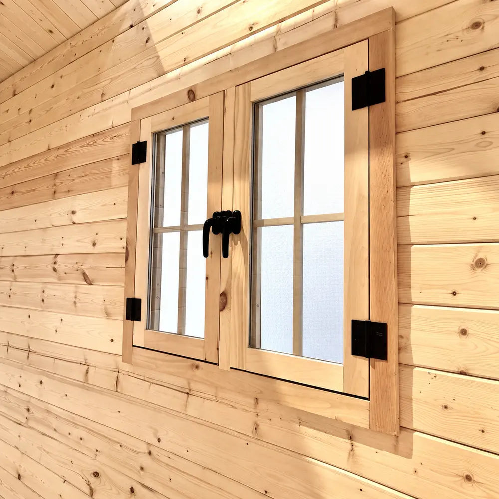 Close-up of a double wooden Multi Cube Versa 100 window with grid panes, black handles and hinges, and sunlit pine framing.