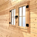 Close-up of a double wooden Multi Cube Versa 100 window with grid panes, black handles and hinges, and sunlit pine framing.