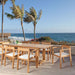 Multiple Westminster Teak Horizon Teak Dining Armchairs surround a large outdoor table on a patio overlooking the ocean, creating a relaxed dining setting