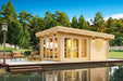 Nestled beside a pond with mountain views, the GardenHouse24 USA Sauna Tanonka 70 Garden Room glows warmly from within its stylish, circular-windowed frame