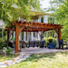 Nestled in a serene garden, the Brookside Timber Frame Highlan Oasis Pergola provides a shaded, stylish retreat with seating, string lights, and an elegant wooden design