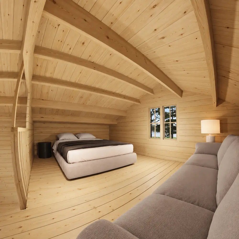 Northwood Grand DD upper loft with a double bed, dark blanket, round bedside table, light-gray couch and exposed wooden ceiling beams.