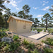 Rear view of the Northwood Grand DD cabin with natural wood siding, small windows and a spacious patio furnished with white chairs and a black firepit.