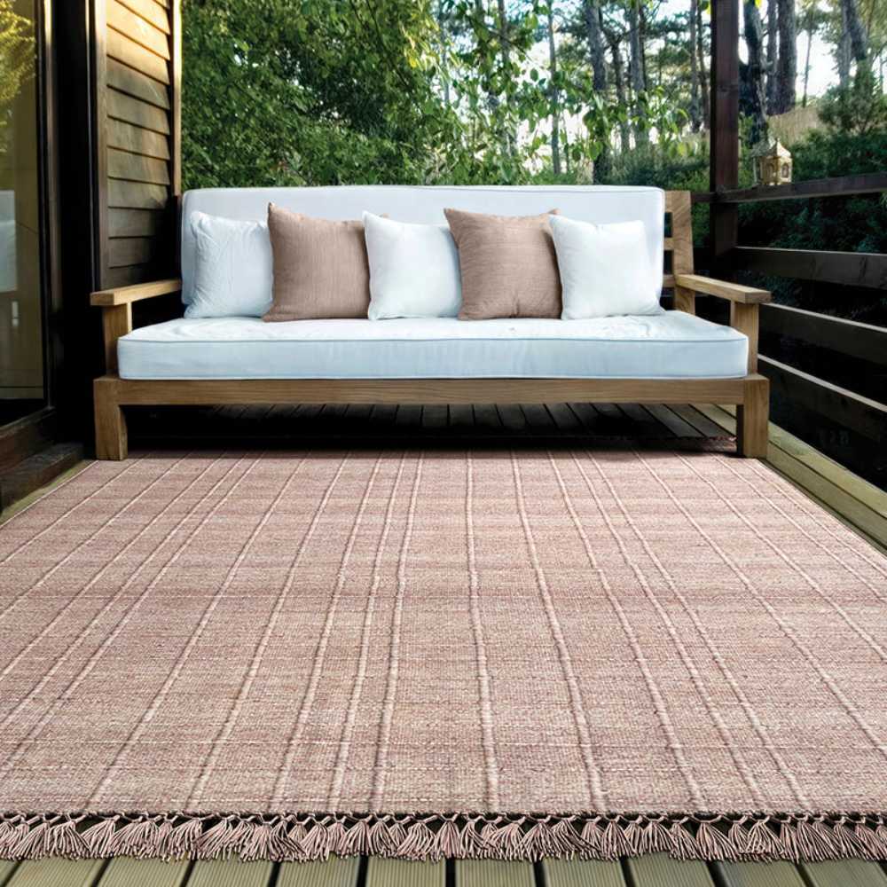 On a wooden patio, the Couristan Ascot Indoor/Outdoor Rug - Windowpane/Rose sits under a cushioned bench, adding cozy charm to the outdoor setting