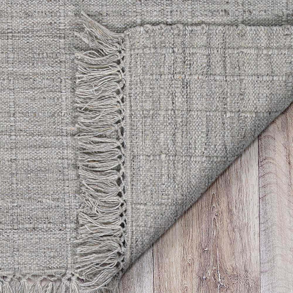 One corner of the Couristan Ascot Indoor/Outdoor Rug - Windowpane/Linen is folded over to reveal the detailed fringe and backside texture on a wood surface