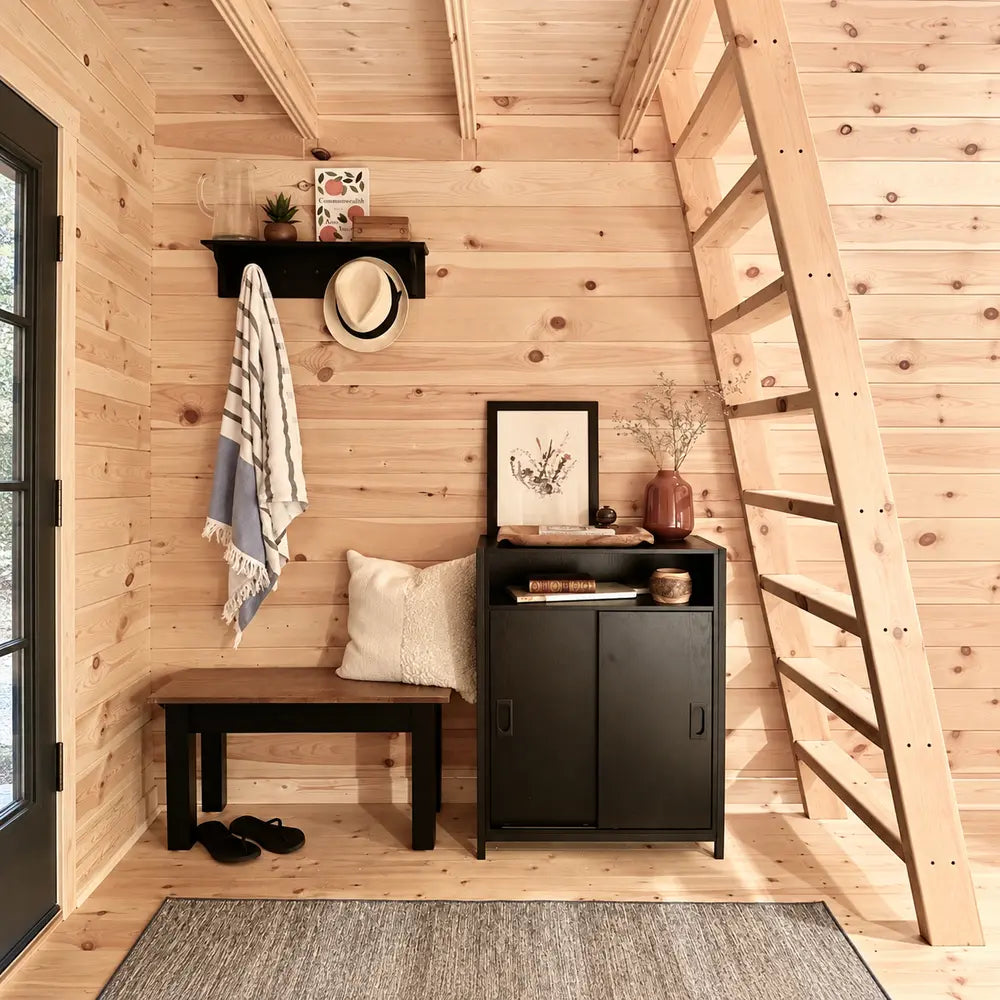 Compact Ontario Grand Loft 107 SD entryway with a black bench and cabinet, wall hooks, round mirror, framed art, and a wooden loft ladder.