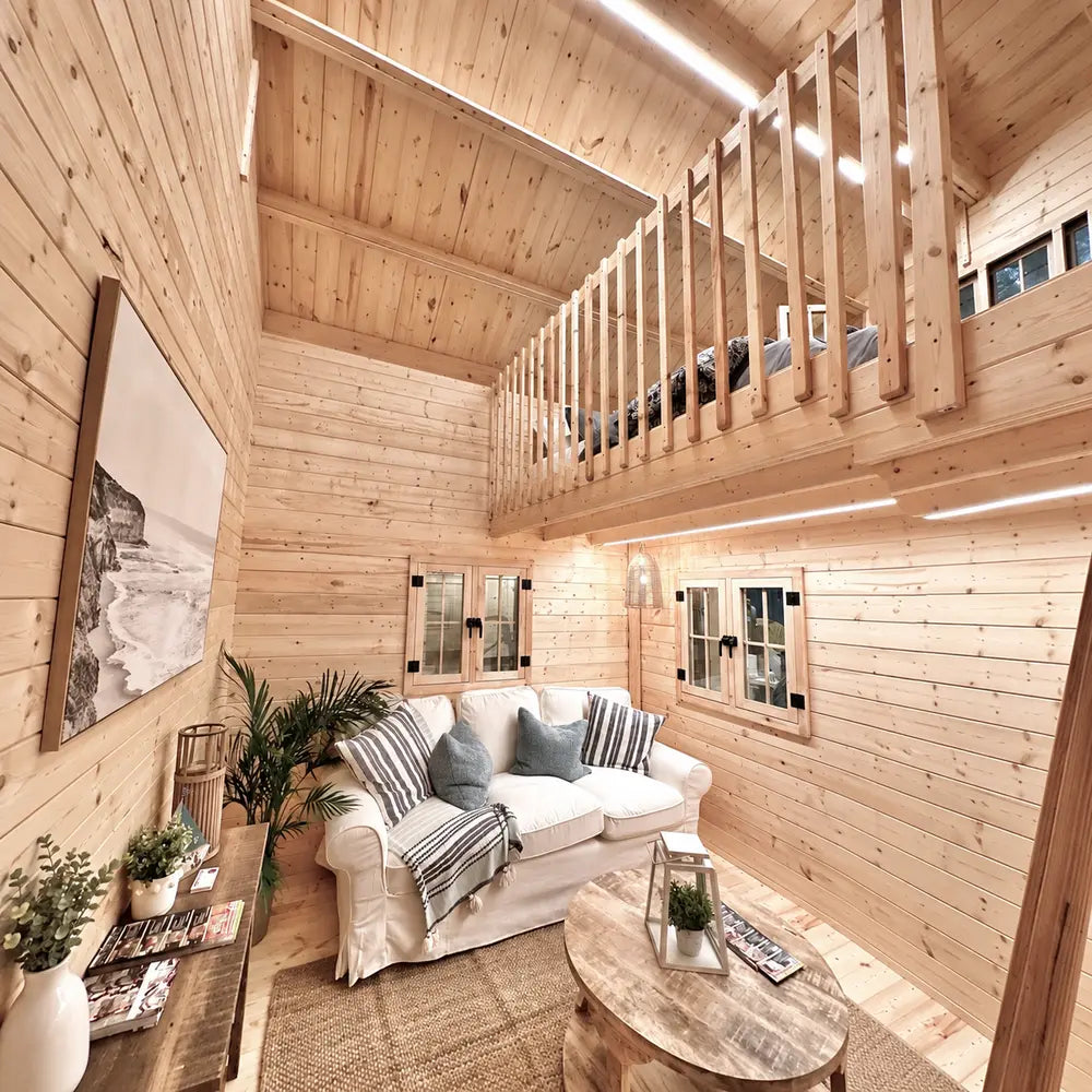 Double-height Ontario Grand Loft 107 SD living room with a white sofa below, wooden loft railing, loft bed, plants, and tall pine walls.