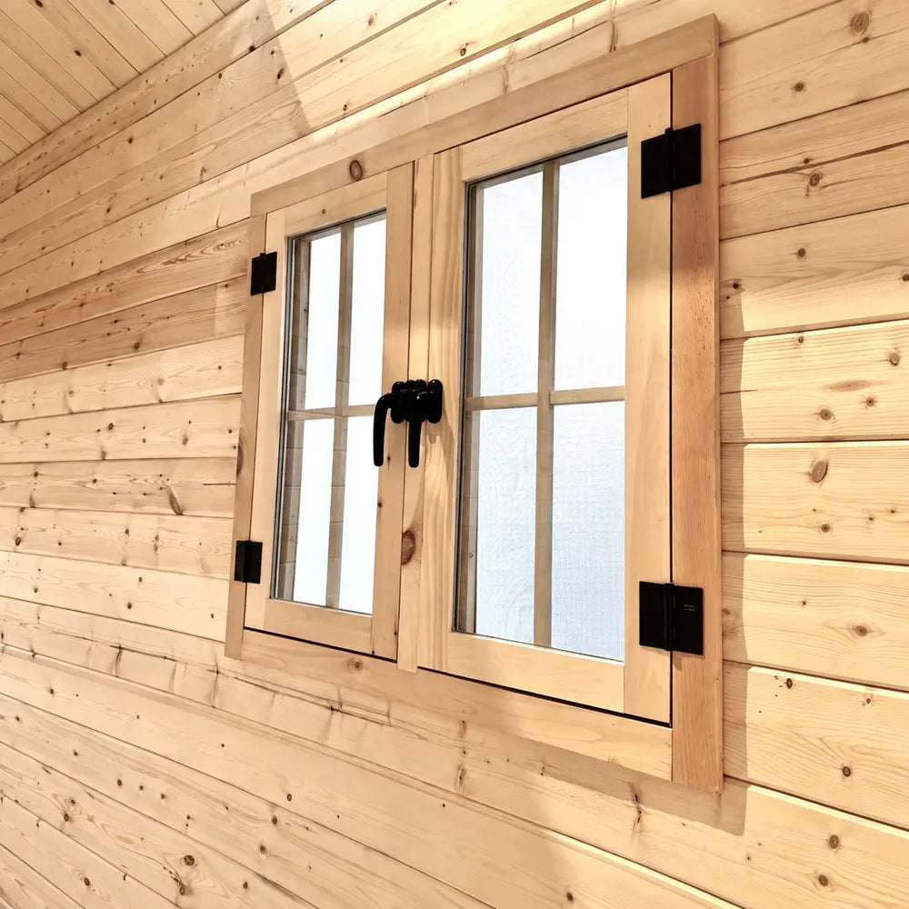 Close-up of a wooden double-paned window with black hinges and handles installed in the pine wall of the Ontario Grand Loft 107 SD.
