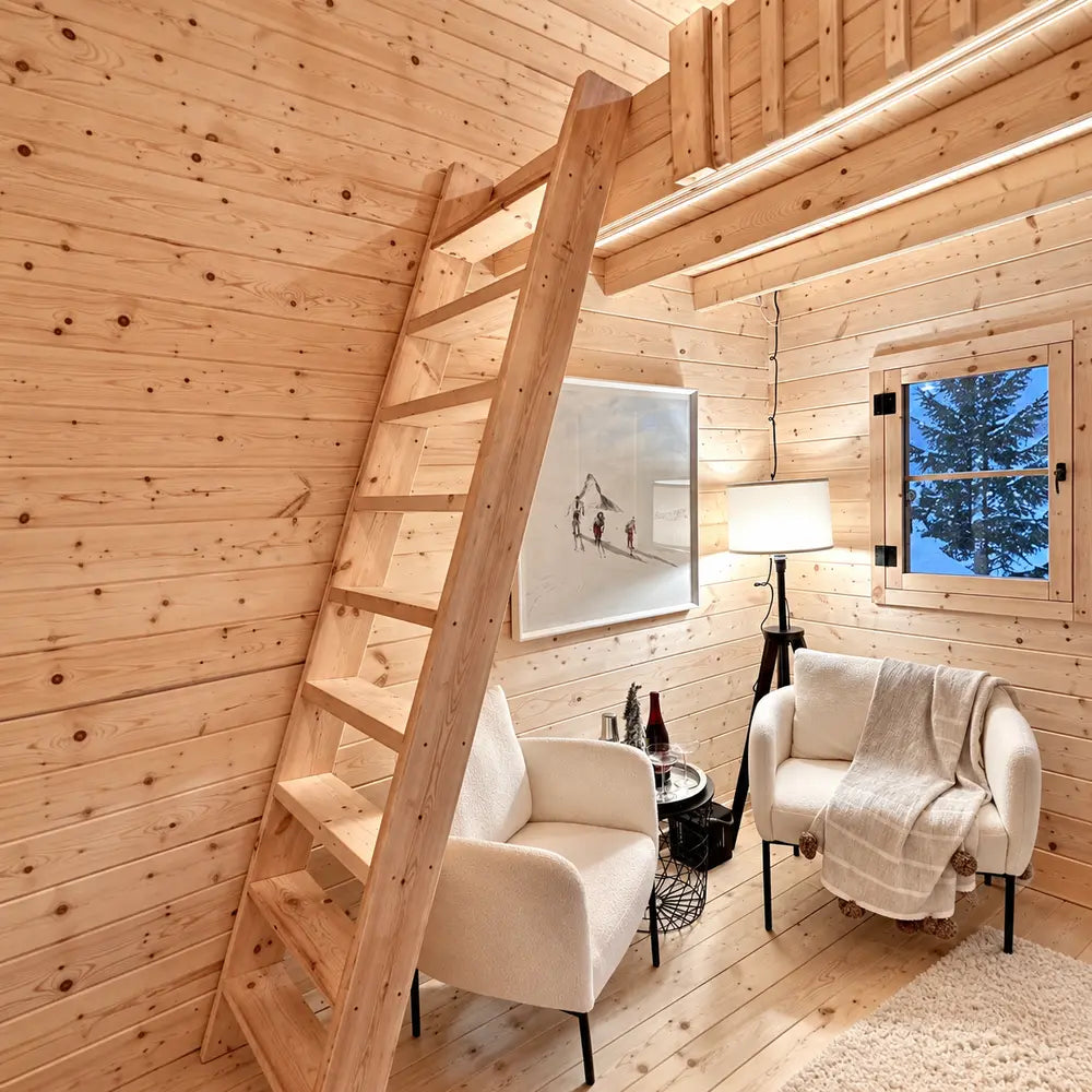 Simple wooden ladder leading to the Ontario Grand Loft 107 SD loft above a cozy sitting area with white chairs and warm lighting.