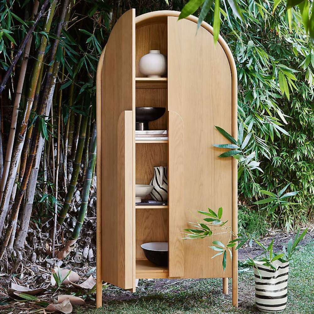 Open Crate & Barrel Annie 38" Natural Storage Cabinet displaying shelves with decorative bowls and books in an outdoor garden setting