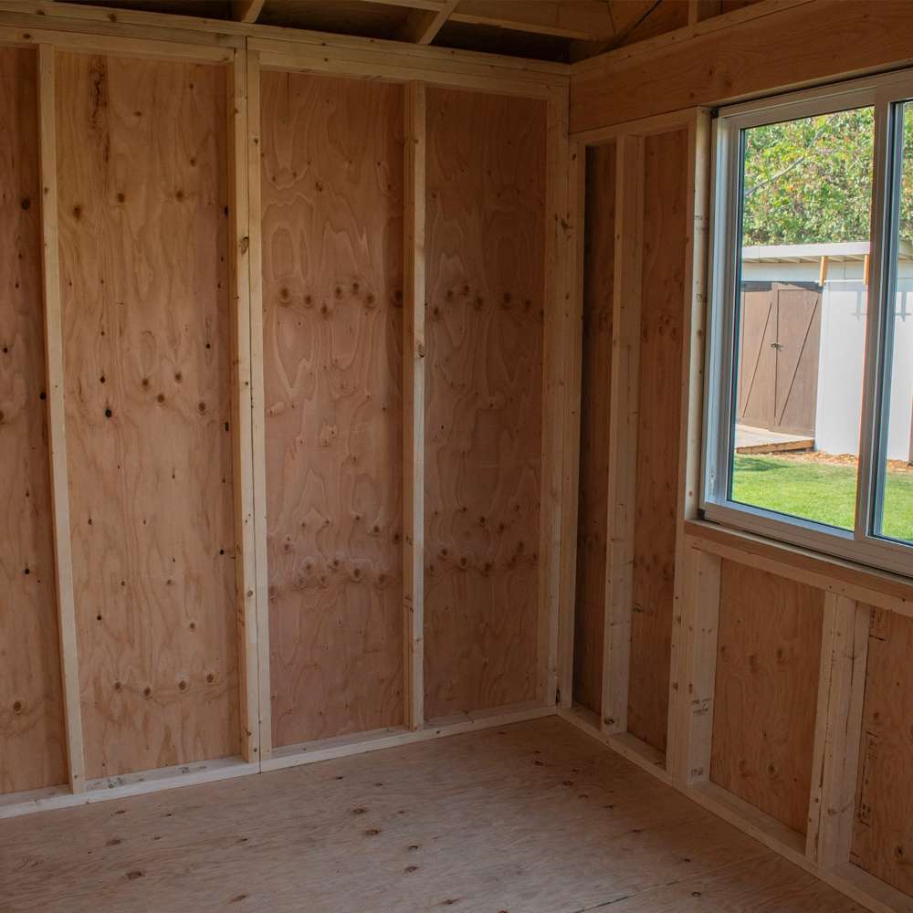 Outdoor Living Today 12×8 Saltbox Studio Outdoor Office is shown as an empty interior corner with exposed wooden framing and a window overlooking a yard