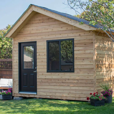 Outdoor Living Today 12×8 Saltbox Studio Outdoor Office is shown in a front angled view with a black door, window, and potted flowers beside the structure