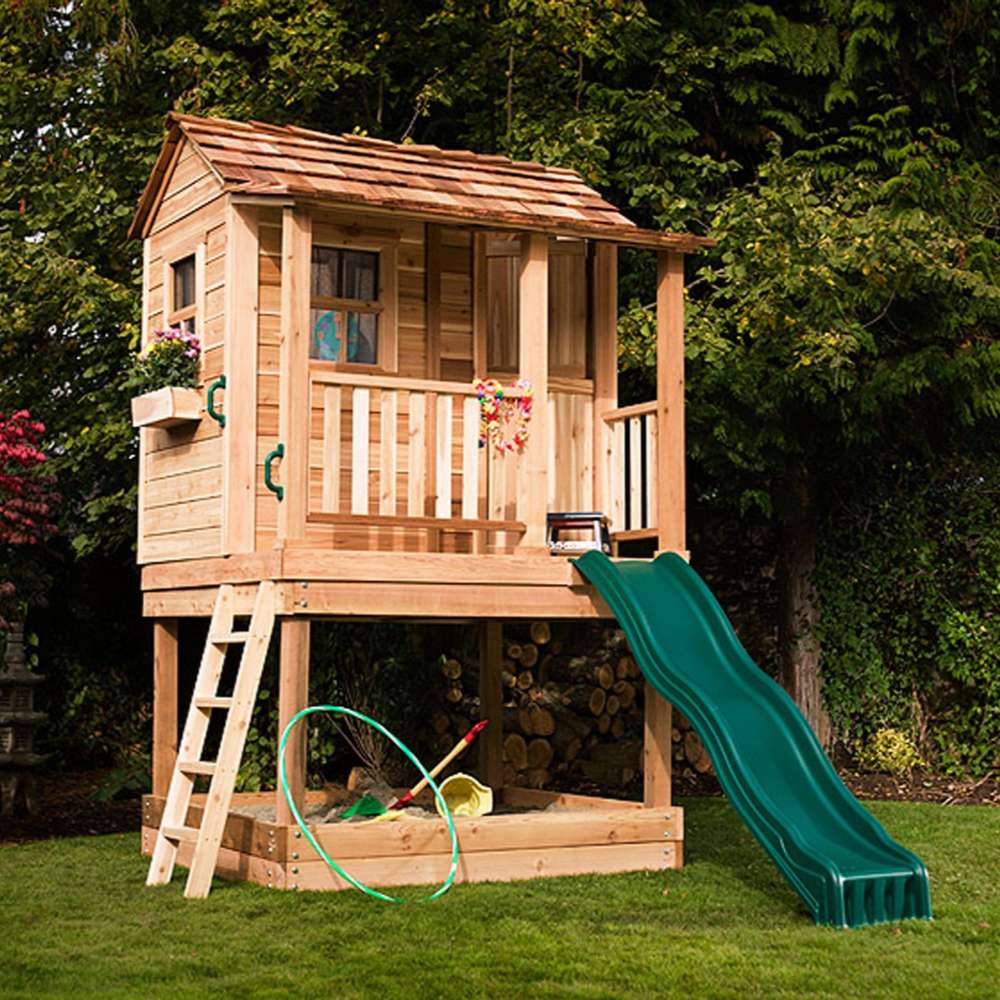 Outdoor Living Today 6x6 Little Cedar Playhouse & Sandbox features a compact wooden playhouse with a green slide and built-in sandbox on grass