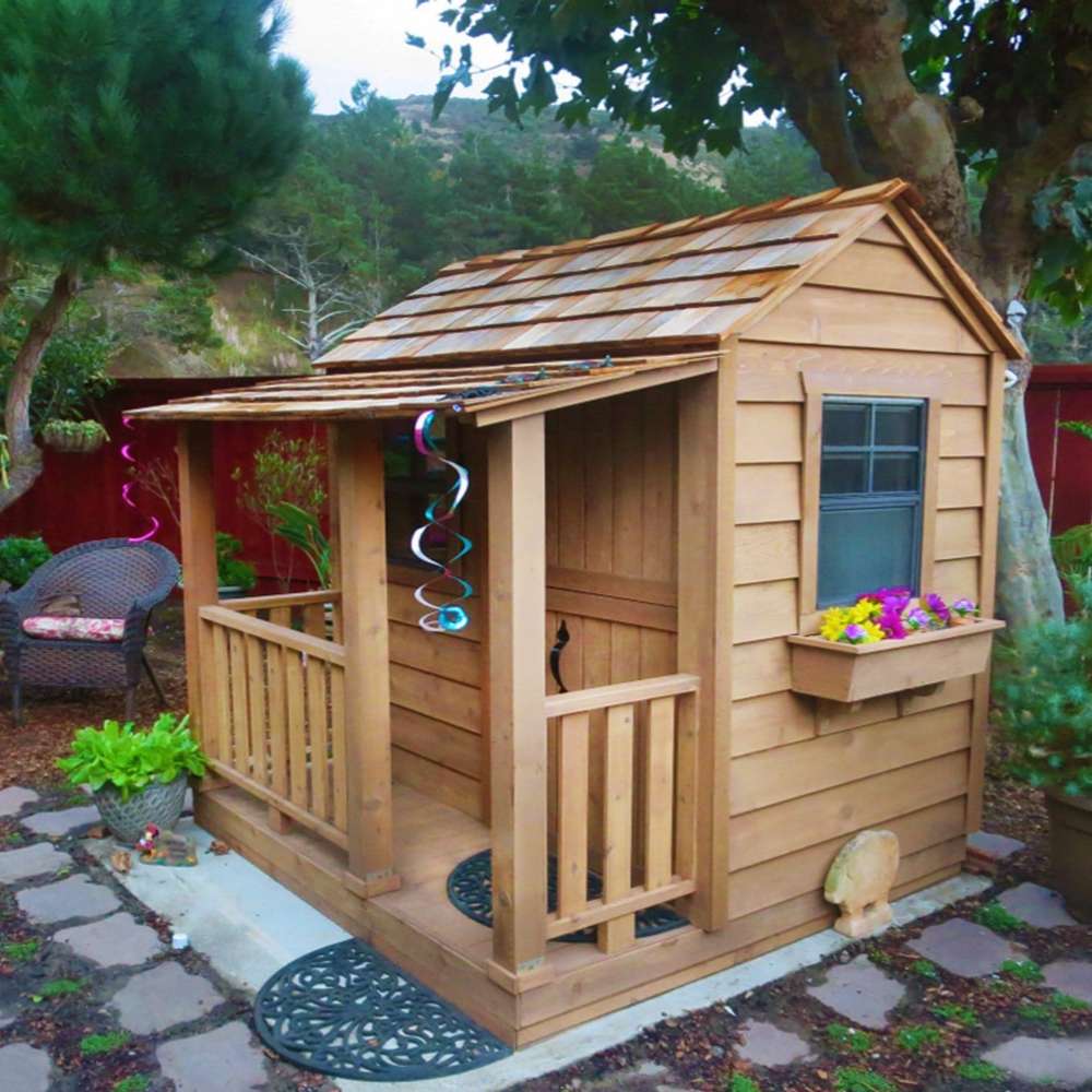 Outdoor Living Today 6x6 Little Cedar Playhouse & Sandbox features a cozy cedar playhouse with a front porch, flower box, and garden surroundings