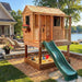 Outdoor Living Today 6x6 Little Cedar Playhouse & Sandbox features a lakeside setup with a green slide leading into a toy-filled sandbox
