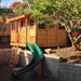 Outdoor Living Today 7x9 Cozy Cabin Signature Cedar Playhouse & Sandbox with elevated design, porch entry, ladder access, and attached green slide