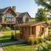 Outdoor Living Today 7x9 Cozy Cabin Signature Cedar Playhouse & Sandbox with natural cedar finish, front porch, and flower boxes set in a landscaped backyard near a large home