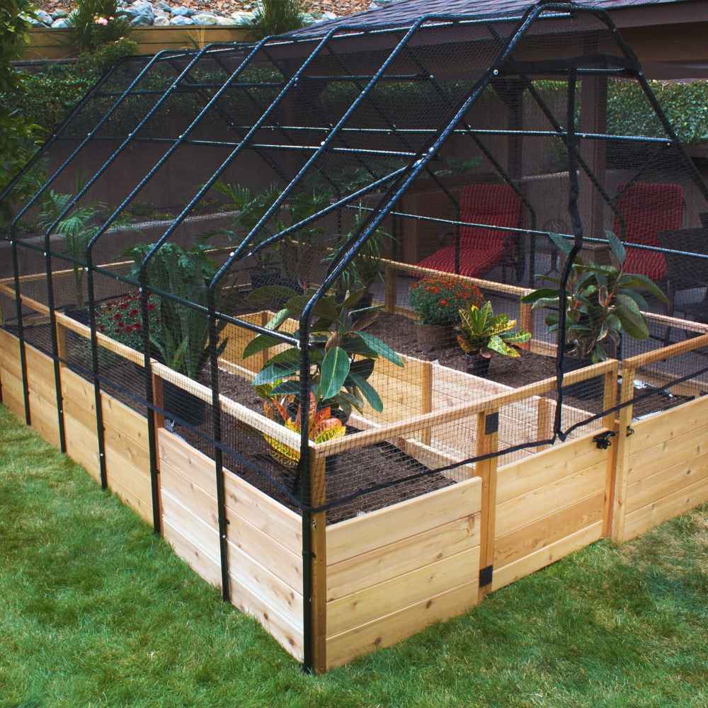 Outdoor Living Today 8×12 Raised Garden Bed sits on a grassy yard with a black mesh cover arching over potted plants and garden beds inside