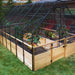 Outdoor Living Today 8×12 Raised Garden Bed sits on a grassy yard with a black mesh cover arching over potted plants and garden beds inside
